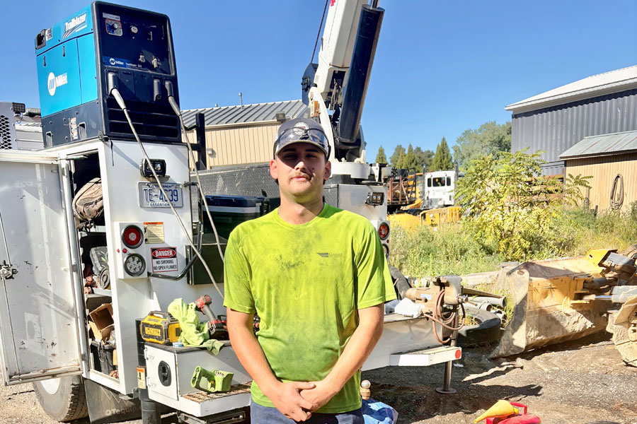 Gaines and Company Mechanic Noah Geiman stands in front of a trailer with tools and equipment